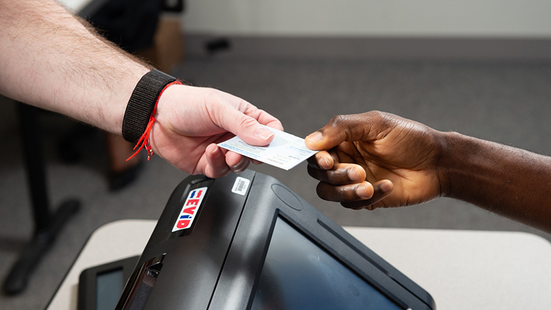 A voter handing an elections poll worker an ID card.