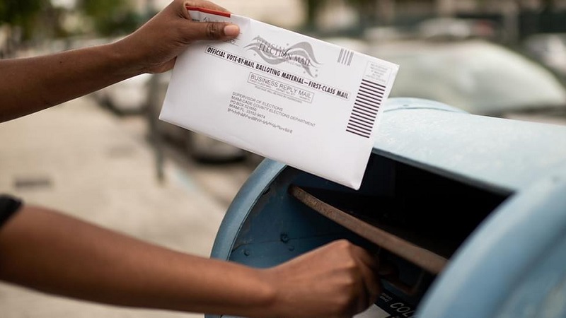 A person dropping a vote-by-mail ballot in a mailbox.